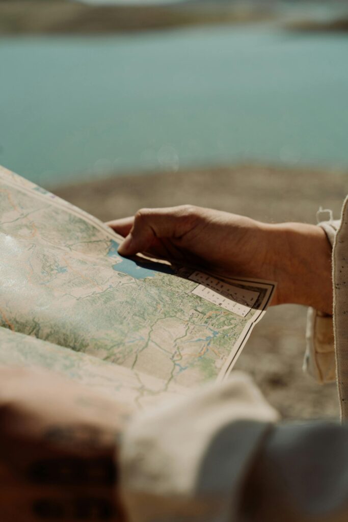 pexels-photo-9909225-9909225 Hands holding a map outdoors with a scenic lake and landscape view in the background.